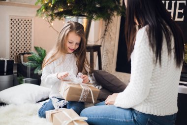 Mutlu Noeller ve mutlu tatiller. Neşeli anne ve tatlı kızı Noel hediyesini açıyorlar. Ebeveynler ve küçük çocuklar Noel ağacının yanında eğleniyorlar.