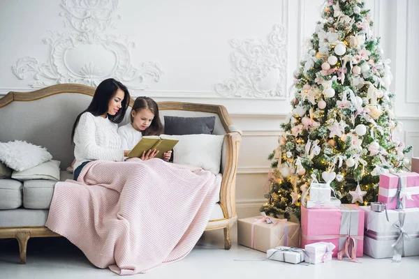 Duas meninas felizes, mãe e filha sentadas em um sofá no quarto decorado de Natal. — Fotografia de Stock