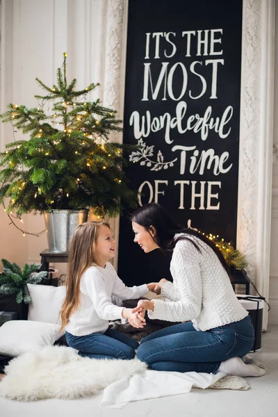 Photo en gros plan de la petite fille en pull tricoté embrasser sa mère alors qu'elle était assise sur le canapé à Noël — Photo