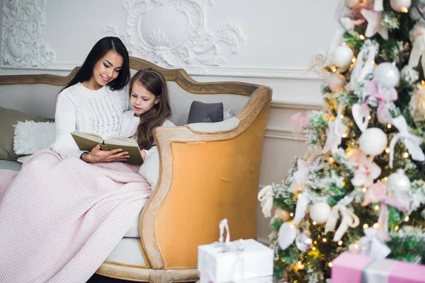 Dos niñas felices, madre e hija sentadas en un sofá en la habitación decorada de Navidad. —  Fotos de Stock