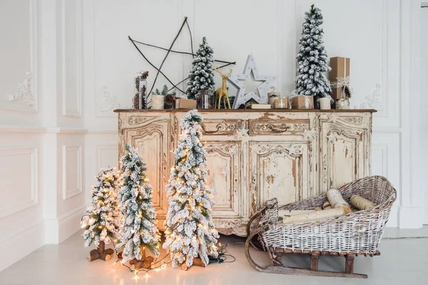 Árbol de Navidad en la cómoda cómoda de madera en el interior blanco, decorado con flores artificiales, guirnaldas y juguetes — Foto de Stock