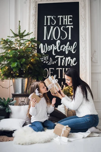 Feliz Natal e Boas Festas. Mãe alegre e sua linda filha menina abrindo um presente de Natal. Pais e criança se divertindo perto da árvore de Natal dentro de casa — Fotografia de Stock