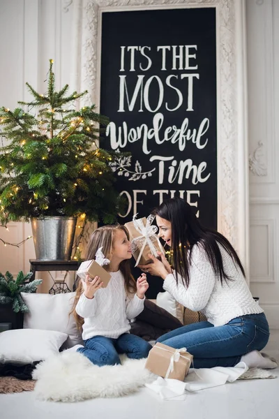 Joyeux Noël et Joyeuses Fêtes. Joyeux maman et sa fille mignonne fille ouvrant un cadeau de Noël. Parent et petit enfant s'amusent près de l'arbre de Noël à l'intérieur — Photo