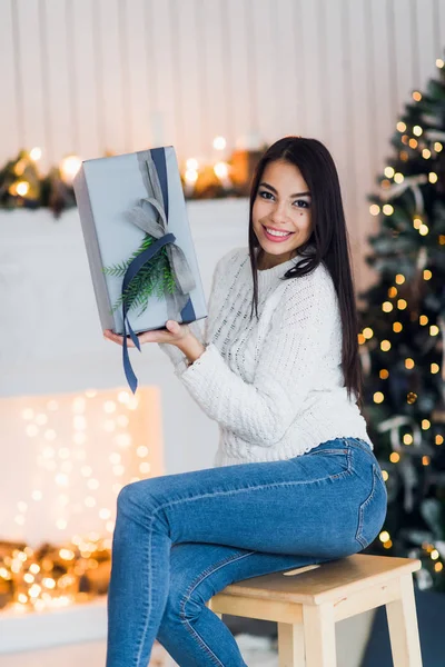 Щаслива молода жінка з різдвяним подарунком здивована і схвильована сидінням вдома проти різдвяних прикрас — стокове фото