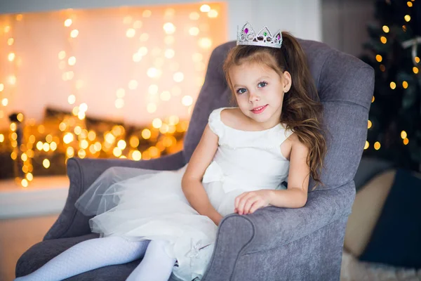 Schattig klein meisje in slimme witte jurk Kerstmis rond de open haard die versierd met vakantie slinger — Stockfoto