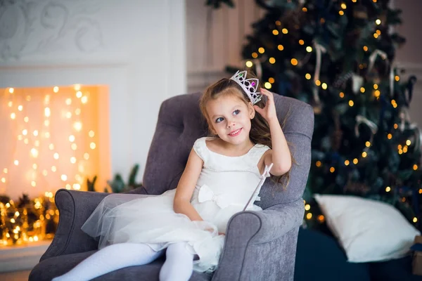 Schattig klein meisje in slimme witte jurk Kerstmis rond de open haard die versierd met vakantie slinger — Stockfoto