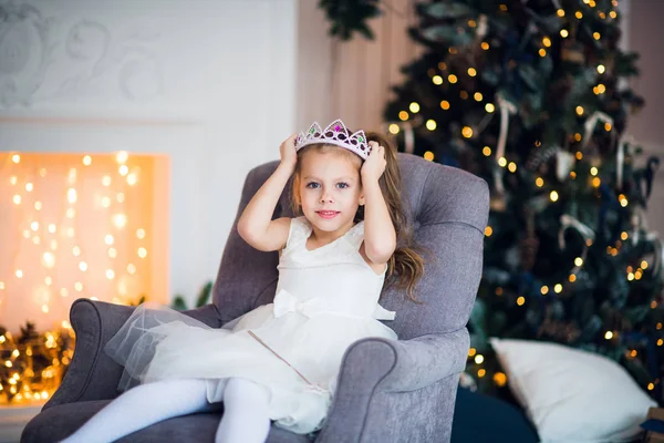 Schattig klein meisje in slimme witte jurk Kerstmis rond de open haard die versierd met vakantie slinger — Stockfoto