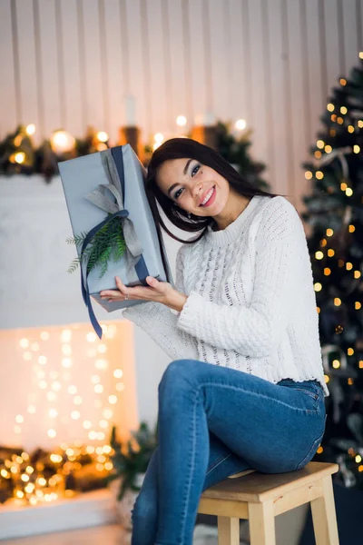クリスマスツリーと暖炉の前に家に座っているクリスマスプレゼントを開くために興奮した幸せな女性 — ストック写真