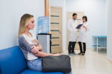 Genç kadın iki doktor bir kağıt üzerinde konuşma sırasında bekleyen hastane koridor az gergin oturma doldurma