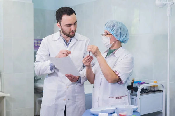 Químicos jóvenes y mayores trabajando juntos y mirando un tubo de ensayo en un laboratorio clínico — Foto de Stock