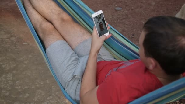 Man met mobiele slimme telefoon terwijl u ontspant in een hangmat — Stockvideo