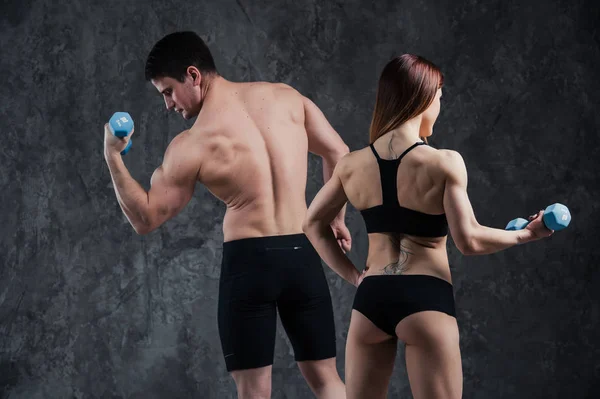 Atraktivní fitness pár sportovní muže drží činku a štíhlá blonďatá žena drží činky nad šedým pozadím — Stock fotografie