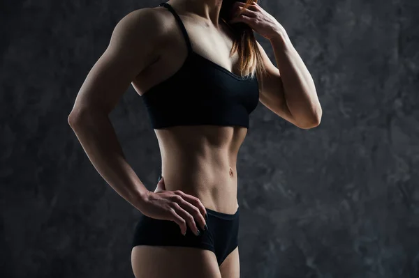 Zijaanzicht van gespierde fitness vrouwelijke model staande op zwarte achtergrond. Jonge vrouw sport-BH in gedachte neerkijkt dragen. — Stockfoto
