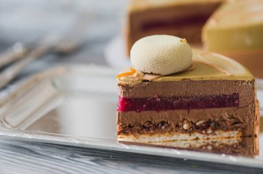 Badem dacquoise, ahududu confit, gevrek katmanla karamelize fındık ve ahududu tozu ile sarı puding kek fırından yeni çıkmış, ahşap masaya servis bağlı olarak bitter çikolata mousse