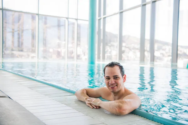 Hombre joven relajándose en una piscina de lujo en la azotea y sonriendo a la cámara en el spa del hotel de cinco estrellas — Foto de Stock