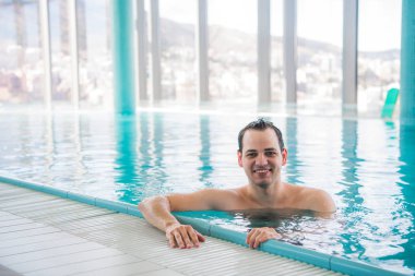 Lüks çatı yüzme havuzu üzerinde rahatlatıcı ve beş yıldızlı otel spa kameraya gülümseyen genç adam