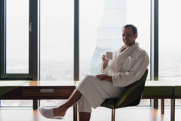 man in bathrobe drinks coffee in luxury hotel in the morning looking at camera
