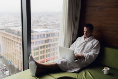 Genç adam evde dizüstü bilgisayarla çalışıyor.