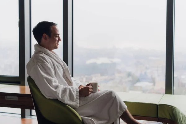 Man in badjas koffie drinken, kijken naar stadsgezicht — Stockfoto