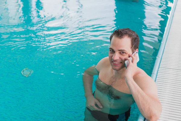 El hombre usa el celular en el borde de la piscina — Foto de Stock