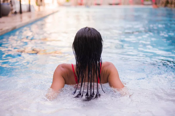 Mujer de pelo negro acostada en el borde del bassin de una piscina con agua azul profunda y fresca ondulada — Foto de Stock