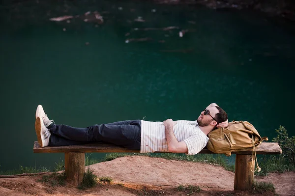 Randonneur homme élégant couché sur un banc en bois près du lac — Photo