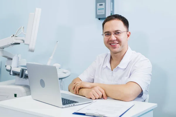 Χαρούμενος ο γιατρός κάθεται στο γραφείο ιατρών με φορητό υπολογιστή — Φωτογραφία Αρχείου