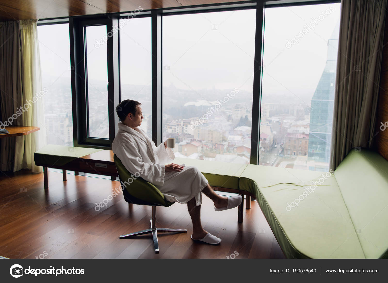 Joven hombre guapo y despreocupado con albornoz cerca de la ventana