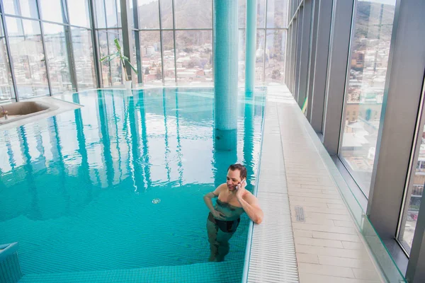 Homem falando no celular dentro da piscina no hotel de luxo — Fotografia de Stock