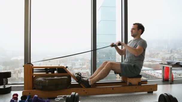 Man op rij machine in fitnessstudio in de fitnessruimte van het hotel van de luxe van het scyscraper uit te werken — Stockvideo