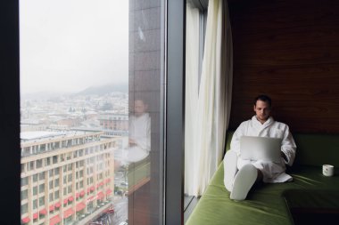 Genç adam evde dizüstü bilgisayarla çalışıyor.