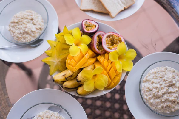 Finom házi reggelit három személy. Oatmeals porrige és a gyümölcs tálban, mangó, banán, passionfruit és virágok. Modern szolgáló — Stock Fotó