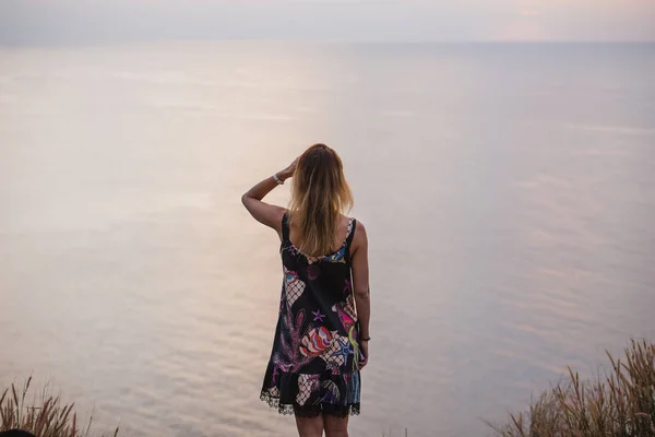 Счастливая женщина в коротком платье наслаждается закатом моря. На заднем плане бесконечная поверхность океана, винтажный цвет — стоковое фото