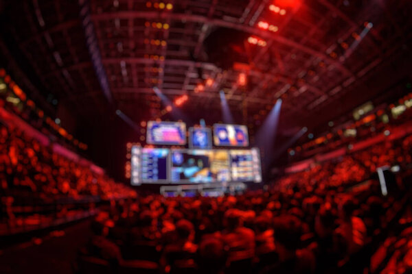 Blurred background of an esports event - Big illuminated main stage of a computer games tournament located on a big stadium. Tribunes are full of video games fans.