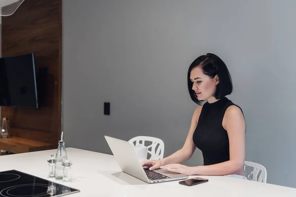 Hermosa mujer de negocios está utilizando un ordenador portátil, mirando a la cámara y sonriendo mientras se sienta en casa — Foto de Stock