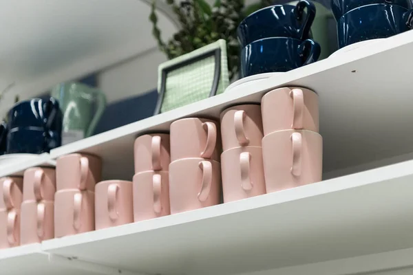 Tasses sur une étagère dans un magasin de cadeaux au détail. Tasses à café rose et bleu foncé sur l'étagère dans la cuisine. Empilement de tasses en céramique sur l'étagère, empilement de tasses à café en céramique propre dans le café . — Photo