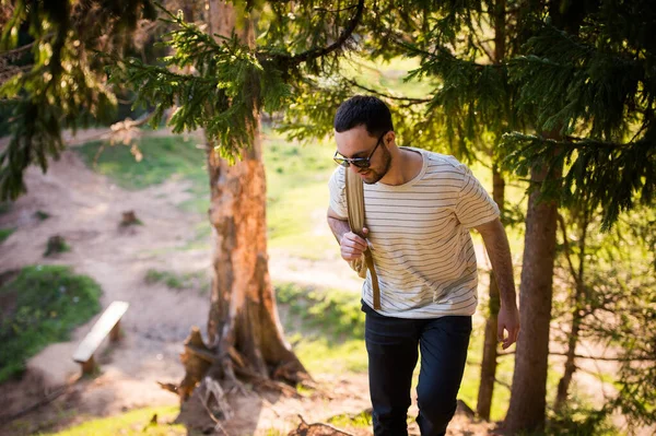 Feliz hombre barbudo viajero con mochila caminando en el bosque. Turismo, viajes, aventura, concepto de caminata - joven sonriente caminando con mochila en el bosque. Concepto de aire limpio y estilo de vida saludable . — Foto de Stock