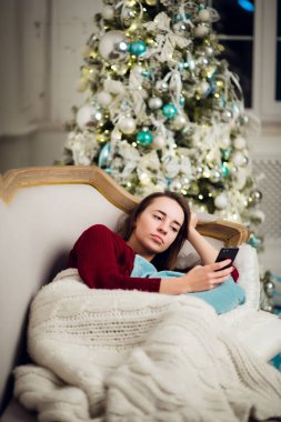 Cep telefonu ev kanepe köknar ağacı önünde yatan genç kadın