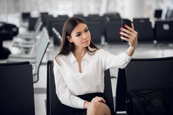 Młoda kobieta na międzynarodowym lotnisku, robi selfie z telefonu komórkowego i czeka na lot. — Zdjęcie stockowe