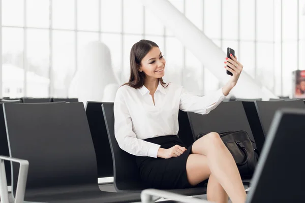 Młoda kobieta na międzynarodowym lotnisku, robi selfie z telefonu komórkowego i czeka na lot. — Zdjęcie stockowe