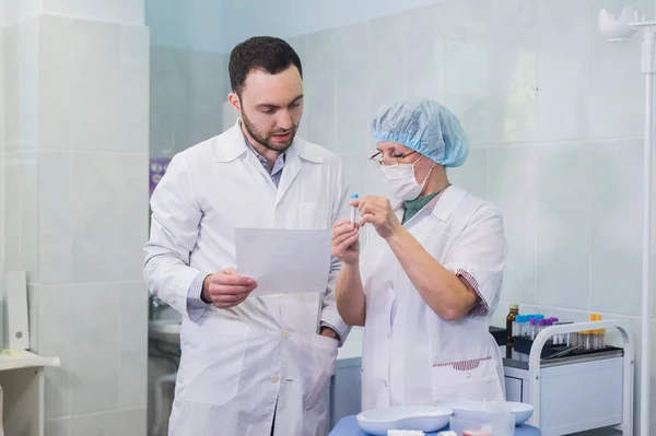 Químicos jóvenes y mayores trabajando juntos y mirando un tubo de ensayo en un laboratorio clínico — Foto de Stock