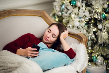 Cep telefonu ev kanepe köknar ağacı önünde yatan genç kadın