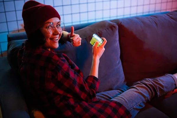 Девочка-подросток держит смартфон, играя в онлайн-игры. Жест вверх пальцами . — стоковое фото