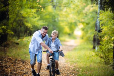 Heyecanlı baba ve oğlu bisiklet kullanmayı öğretmek yeşil parkta birlikte eğleniyor oğlu