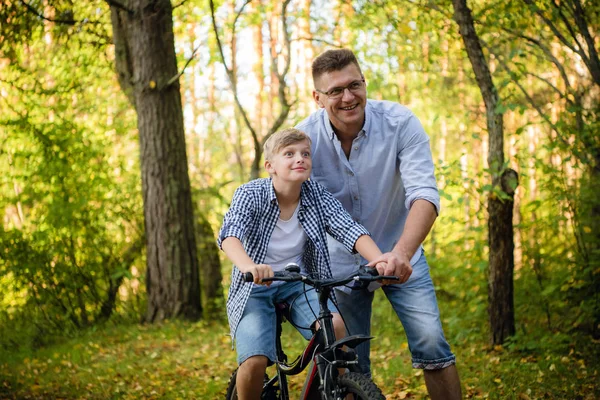 Père excité et son fils s'amusent ensemble au parc vert, apprenant à son fils à faire du vélo — Photo