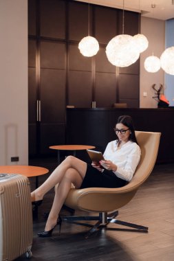 Kendine güveni tam bir iş kadını. Havaalanı iş yerinde sandalyesinde otururken tablet bilgisayarından müzik dinliyor.