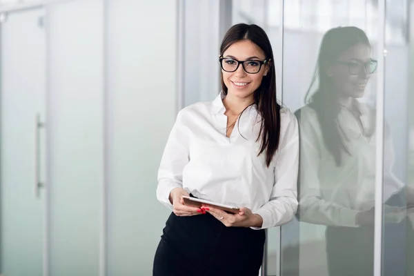 Mujer de negocios con blusa blanca de pie en el pasillo de la oficina con la tableta y sonriendo. —  Fotos de Stock