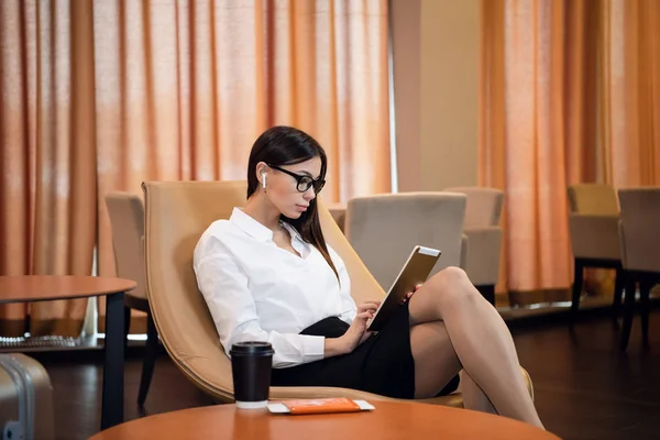Mujer de negocios segura escuchando música en su tableta mientras está sentada en la silla en la sala de negocios del aeropuerto — Foto de Stock