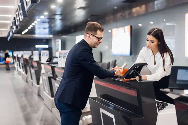 Viaje de negocios. Joven hombre de negocios guapo con su pasaporte y hablando con la mujer en el mostrador de facturación de la aerolínea en el aeropuerto —  Fotos de Stock