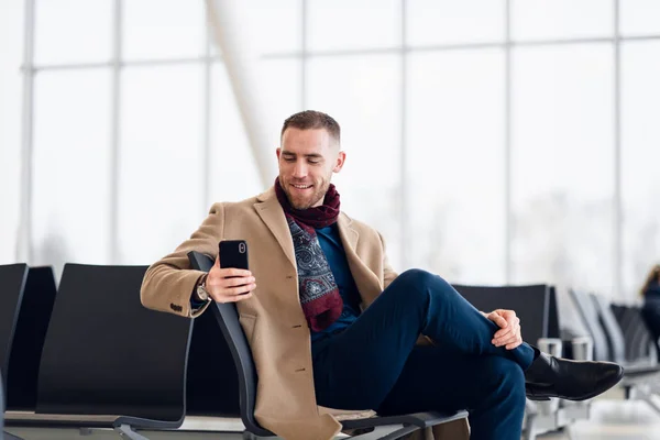 Молодой занятой мужчина ждет вылета в аэропорту, пользуясь телефоном — стоковое фото